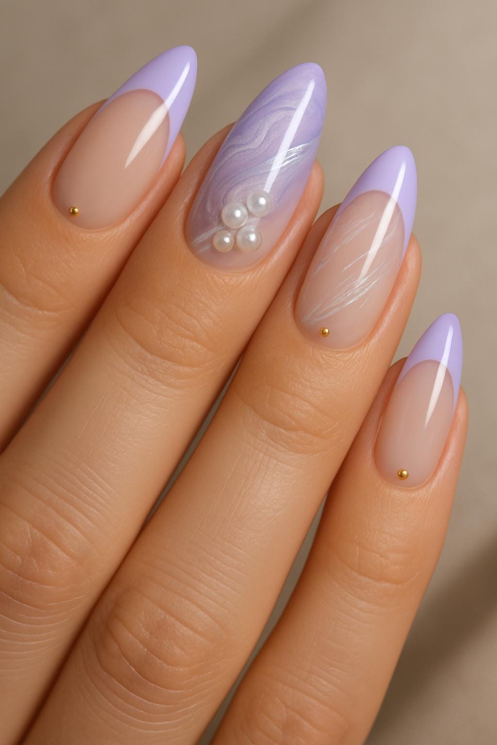 Pastel almond nails with lilac tips, subtle gold studs, and one marbled accent featuring pearly embellishments