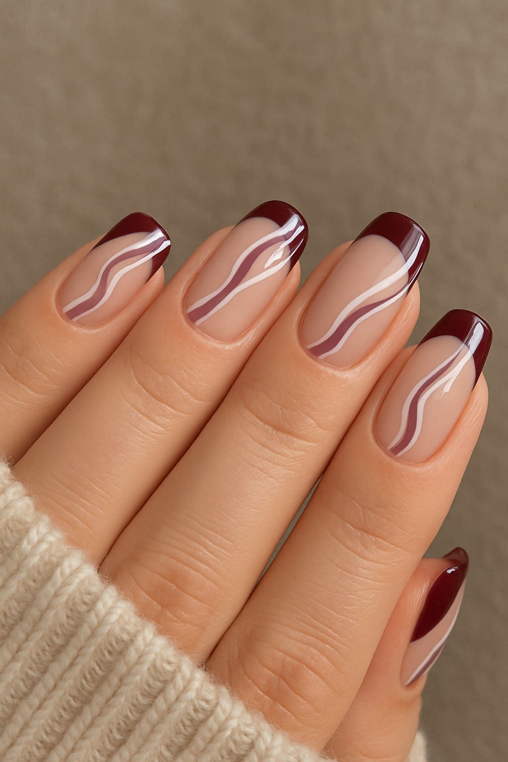 Glossy burgundy French tips with wavy accent lines on nude nails